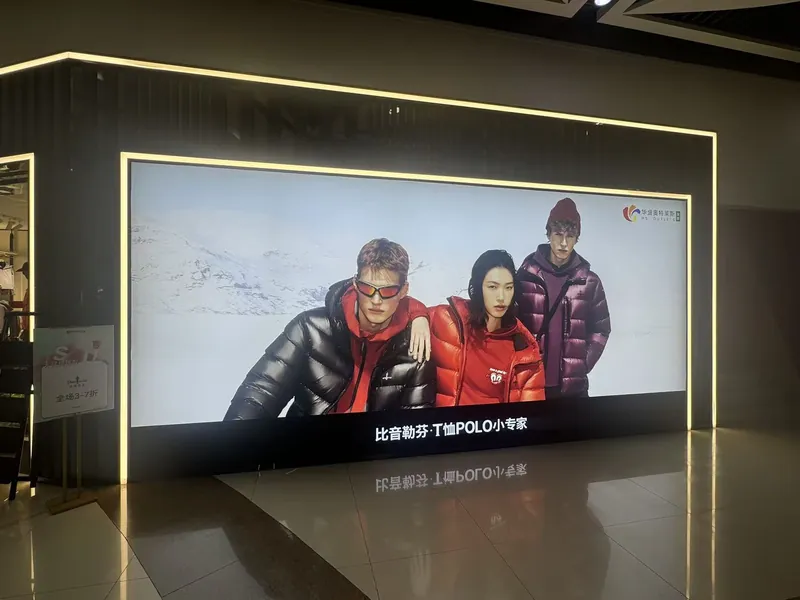 Extra-large fabric lightbox on the storefront of the Biemlofen store at HS Outlets Shenzhen, showing three models in down jackets